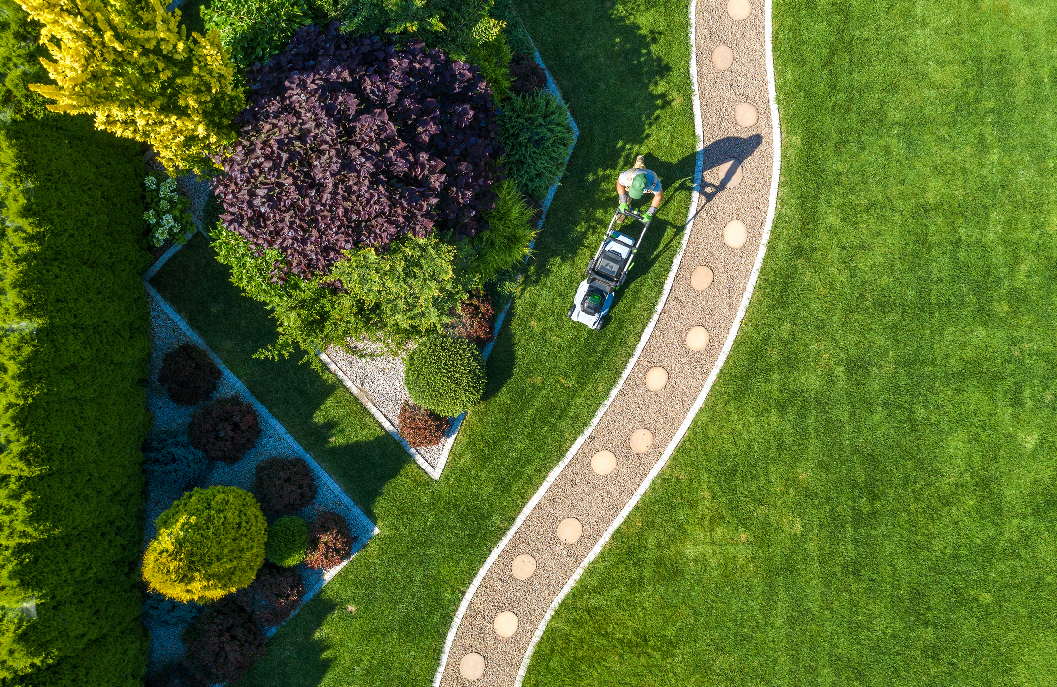 Overhead view of a landscaper mowing a lawn beside trees